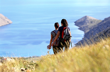 a man and woman walking on a hill overlooking the ocean