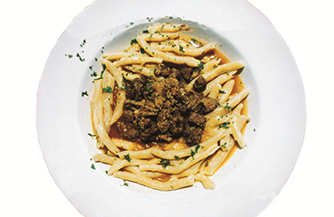 Gekookte pasta (makaruli) gecombineerd met reuzel en kaneel (kanjela) wordt geserveerd met vlees en tomaten, peterselie en knoflook