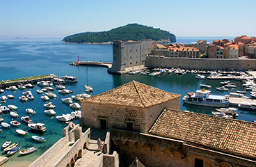 Mestne obzidje Dubrovnika, ki obdaja staro mesto in ponuja razglede na morje in pristanišče, kjer so zasidrane ladje