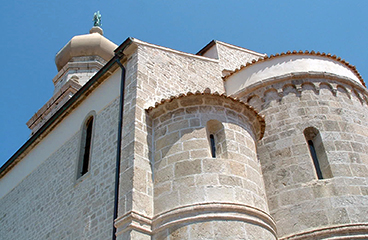 Velicanstvena Katedrala v Krku, zgodovinska kamnita struktura s kompleksnim dizajnom, izstopa na ozadju jasno modrega neba.