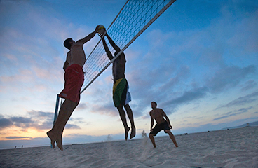 Gruppe von Männern spielt Strandvolleyball in der Dämmerung