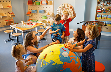 Groep kinderen speelt met een wereldbol in een kinderspeelkamer onder toezicht van getraind personeel