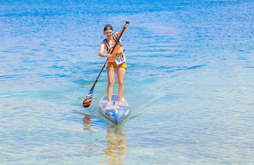 Donna con un giubbotto di salvataggio arancione fa stand up paddle (SUP)