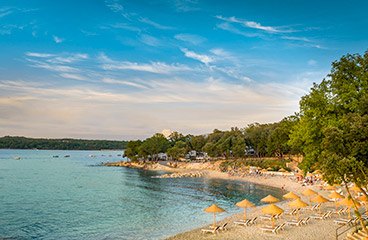 The gentle entrance of the pebbly Val Sunset Family beach, decked with sun loungers and umbrellas