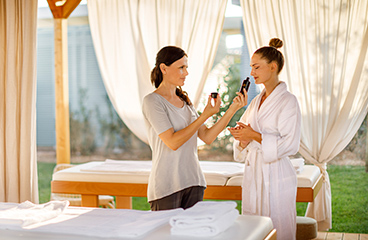 Un massaggiatore offre a una donna, che indossa un accappatoio, una selezione di oli da massaggio aromatici da annusare
