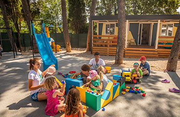 Skupina otrok se igra na otroškem igrišču na prostem pod nadzorom usposobljenega osebja
