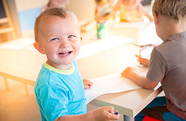 Klein jongetje grijnst terwijl kinderen op de achtergrond tekenen