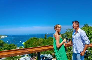 a man and woman standing on a balcony overlooking a beach and ocean