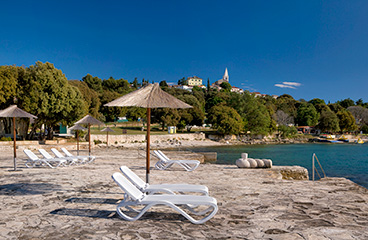 Orsera Camping Resort strand met rotsachtige zonnebad gebieden, enkele kiezels, ligstoelen en parasols