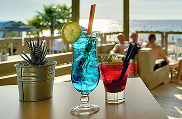 Blauer und roter Cocktail auf einem Tisch in der Petrac Strandbar mit dem Meer im Hintergrund