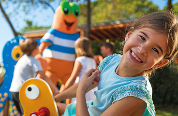 Girl laughing with other children and the Maro mascot in the background