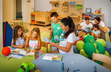 Getraind personeel speelt met kinderen in de zachte speelkamer - moderne speelkamer met verschillende vermakelijke elementen