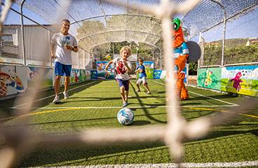 Kinder, die Fußball spielen mit ausgebildetem Personal und der Maskottchen Maro