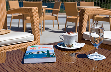 Touristenbuch über Kroatien auf einem Holztisch mit einer Tasse Kaffee daneben
