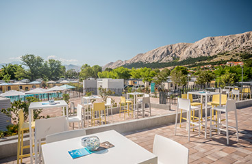a patio with tables and chairs and a mountain in the background