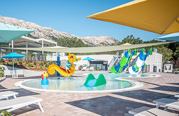 Kinderwaterpark met ondiep verwarmd zwembad, sproeiers en twee waterglijbanen