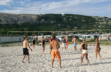 Grupa ljudi igra odbojku na pijesku na terenu